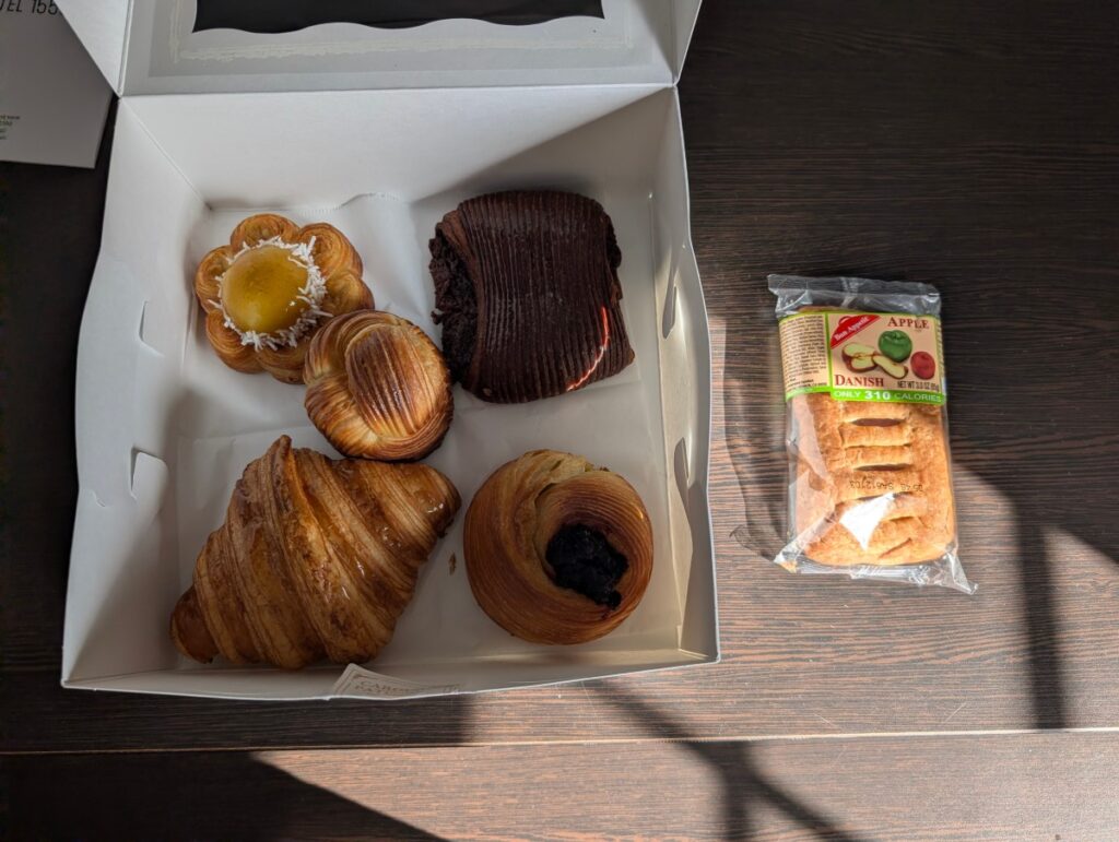 A box of handmade Le Carousel pastries beside a shrink-wrapped supermarket apple danish labelled 310 calories.