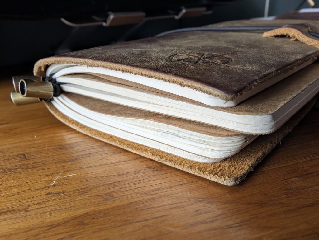 Side view of the Wanderings A6 traveller's notebook overstuffed with four inserts that jut out past the edges of the leather cover.