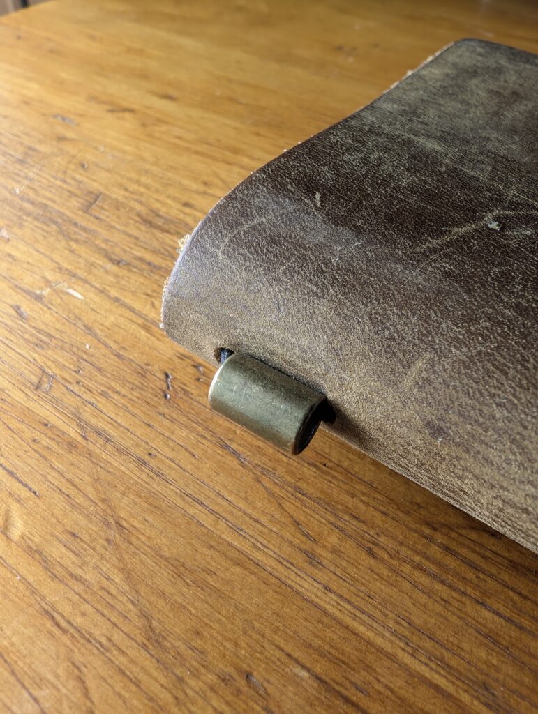 Close-up of a single brass bobble cord end emerging from the spine of the Wanderings A6 traveller's notebook.