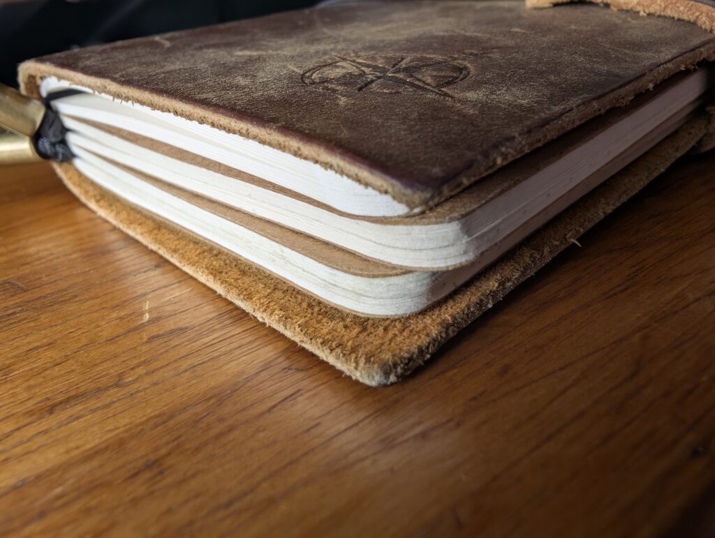 Side view of the Wanderings A6 traveller's notebook showing three inserts stacked inside the single leather strap.